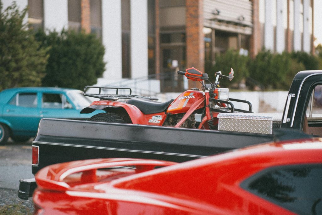Red Honda ATV loaded on a black pickup truck parked in an urban environment.